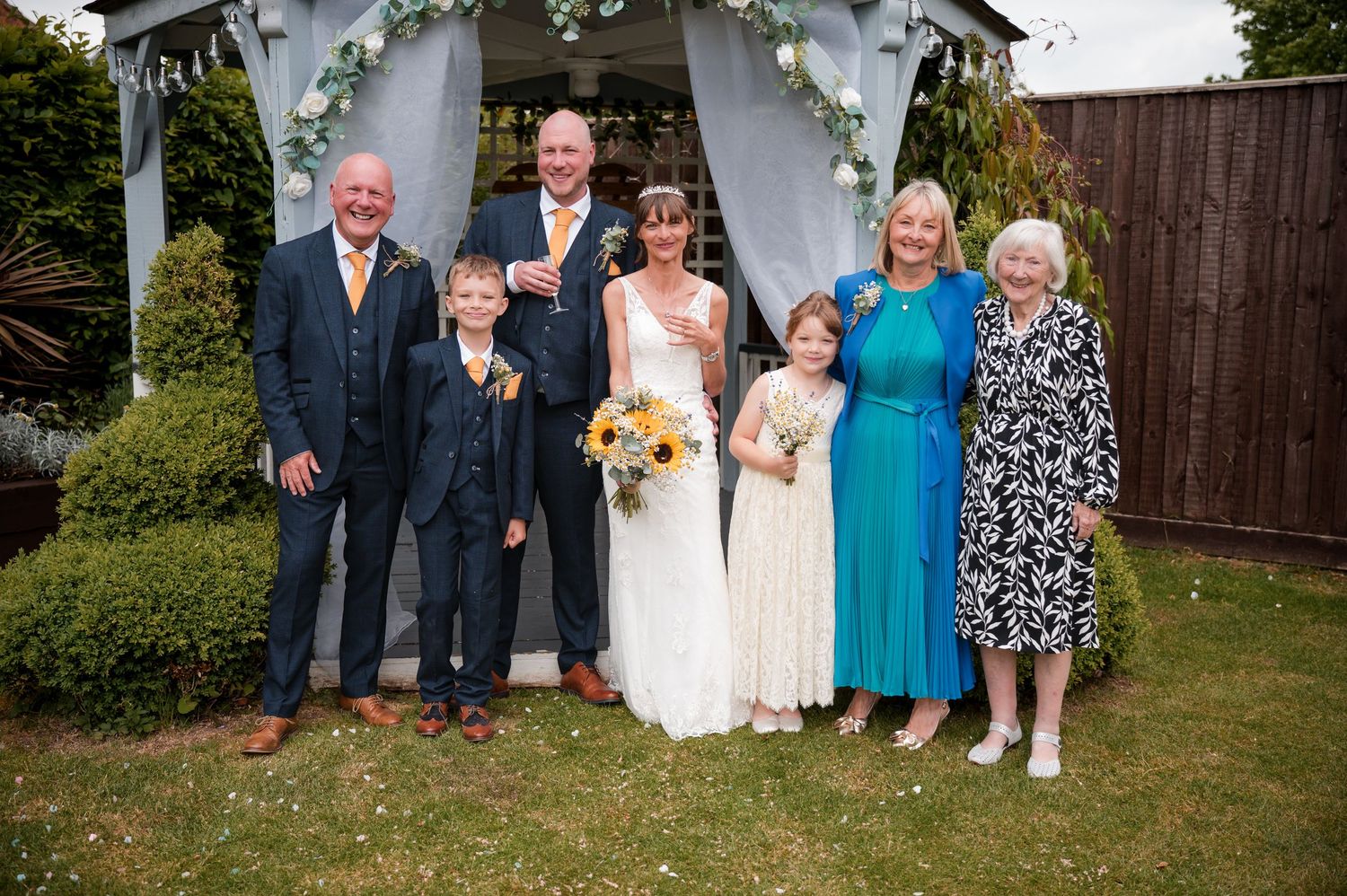 Wedding party members pose together outdoors in formal attire during a garden celebration.