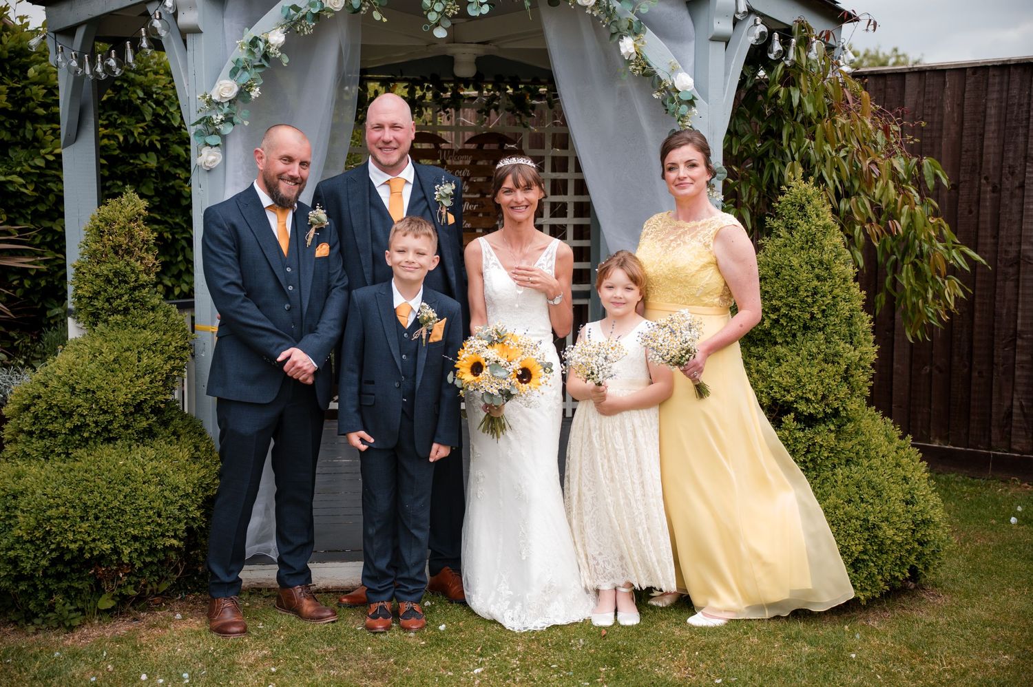 Wedding party members in formal attire pose for photos in an outdoor garden setting.