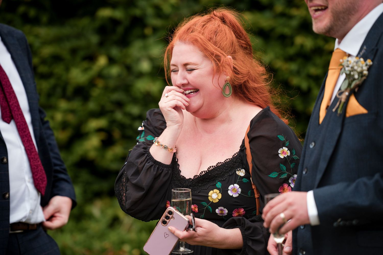 A group of formally dressed people laugh together during an outdoor celebration event.