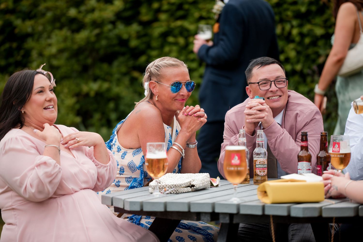 Friends enjoy food and drinks while sitting together at an outdoor table during a sunny gathering.