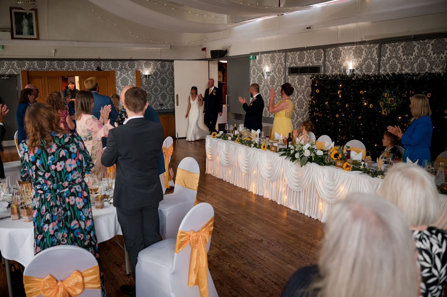 Wedding guests mingle and dance in an elegant reception hall decorated with damask wallpaper and twinkling lights.