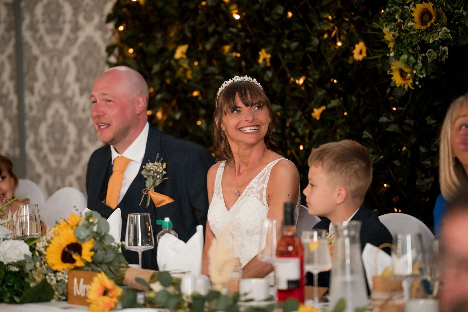 Wedding guests enjoy a festive outdoor reception with sunflowers and string lights creating a warm atmosphere.