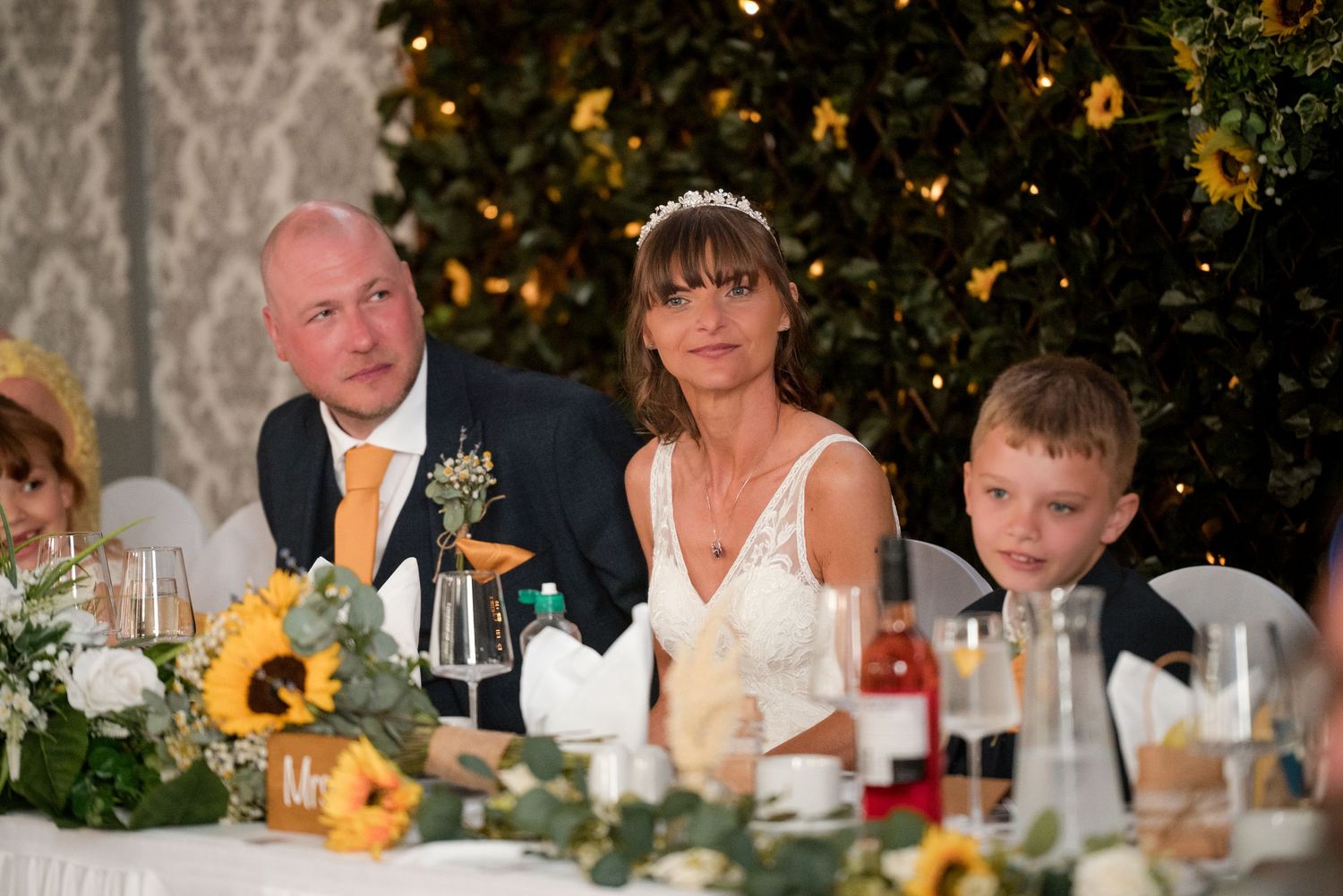Wedding guests seated at a reception dinner table with sunflower decorations and glowing candlelight.