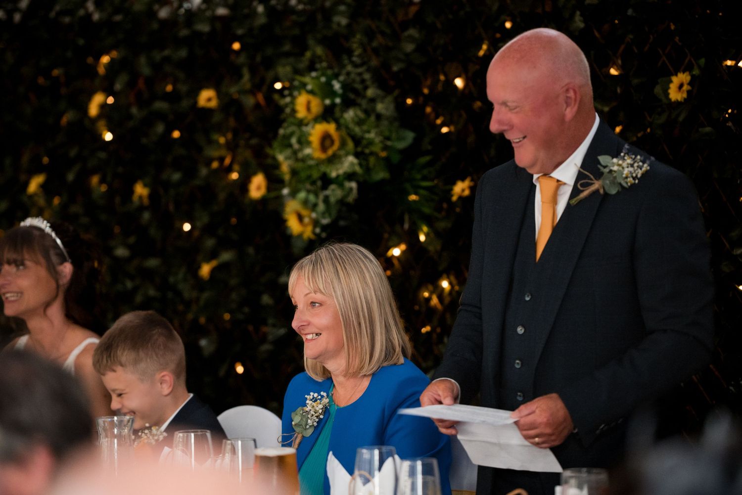 Elegant wedding reception table with guests enjoying dinner under ambient lighting and floral centerpieces.