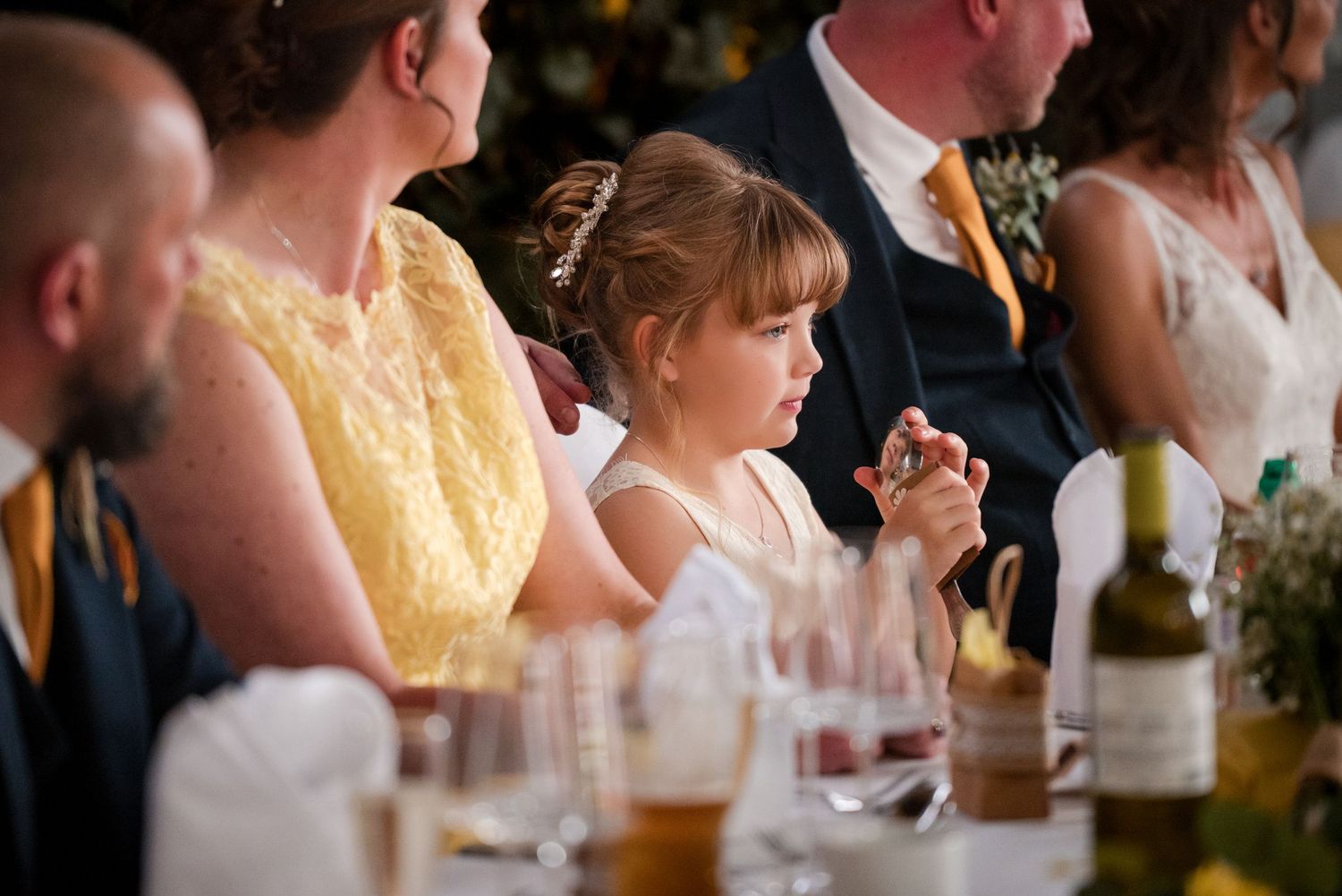Wedding guests seated at a long table during an evening reception with warm lighting and festive decor.