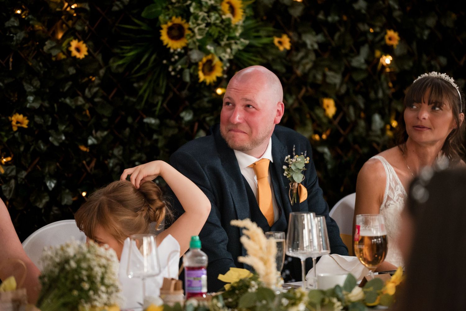 Wedding reception table decorated with sunflowers and greenery under soft evening lighting.