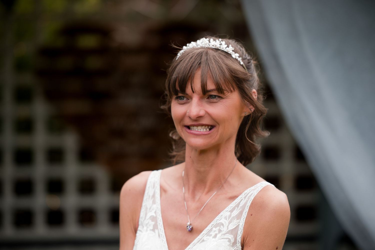 A bride in a white wedding dress smiles while standing in front of a decorative lattice backdrop.