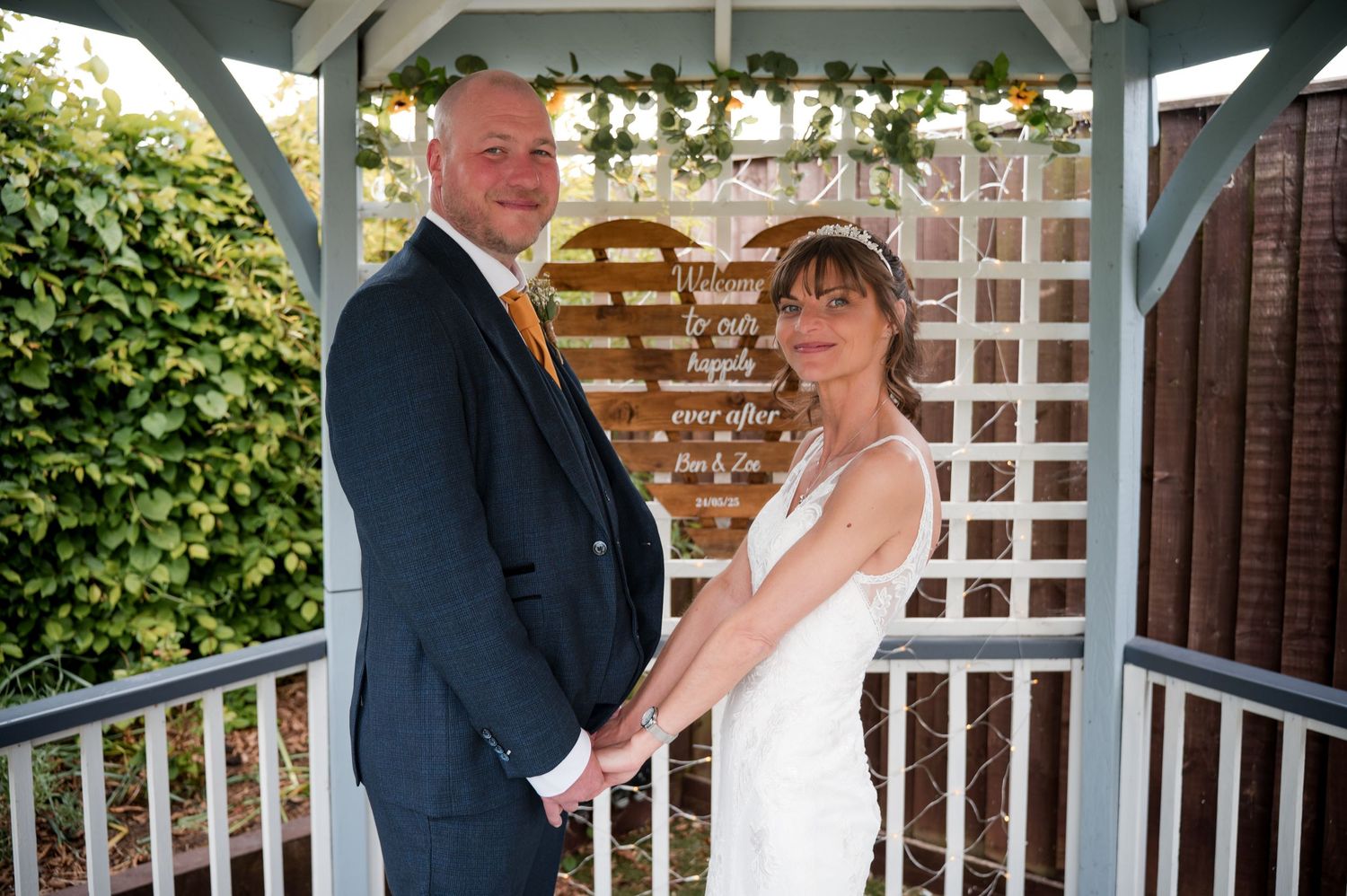 Bride and groom share a romantic moment on a white lattice porch during their wedding celebration.