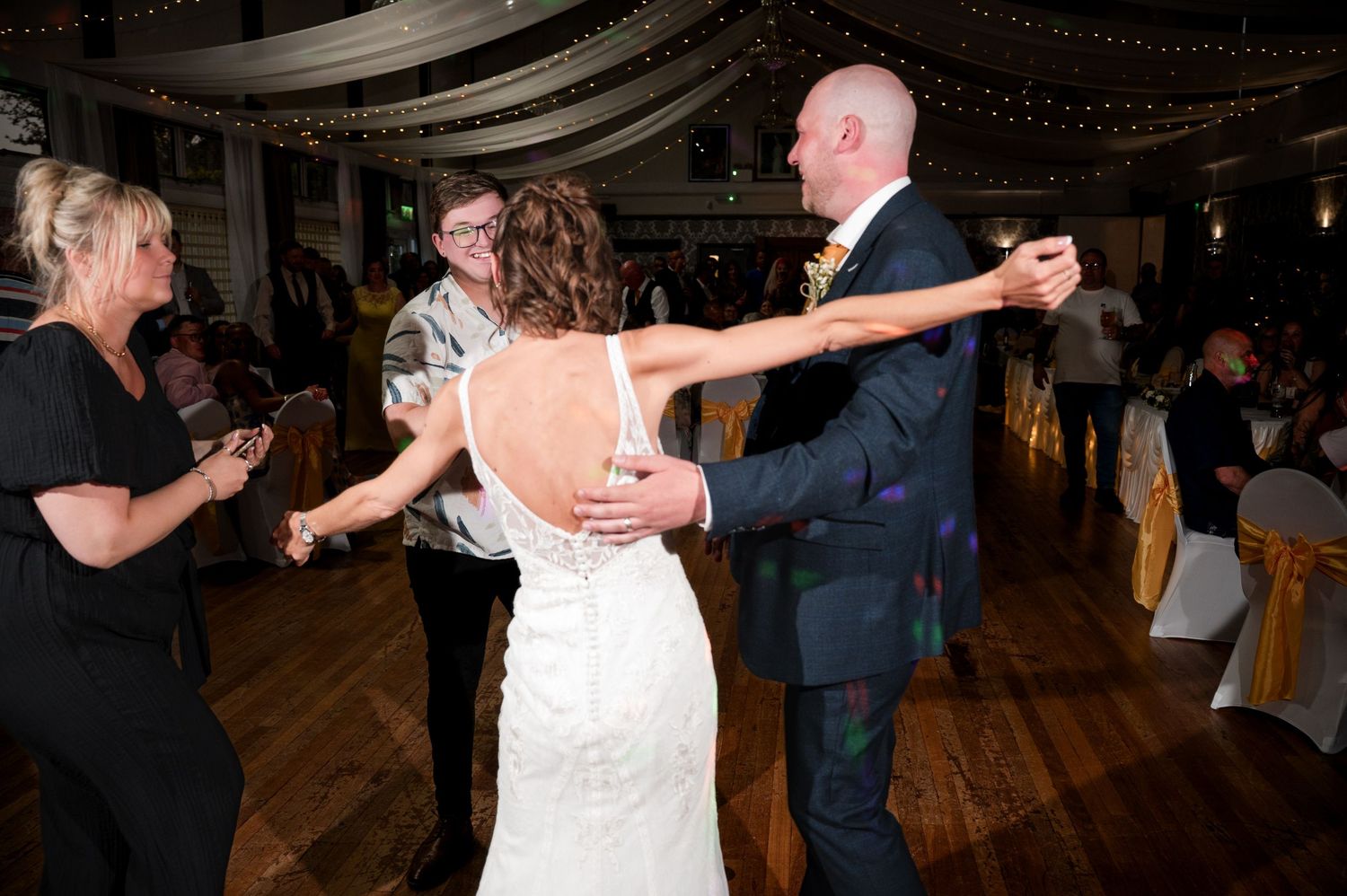 Couple dancing together at a wedding reception on a wooden dance floor with string lights overhead.