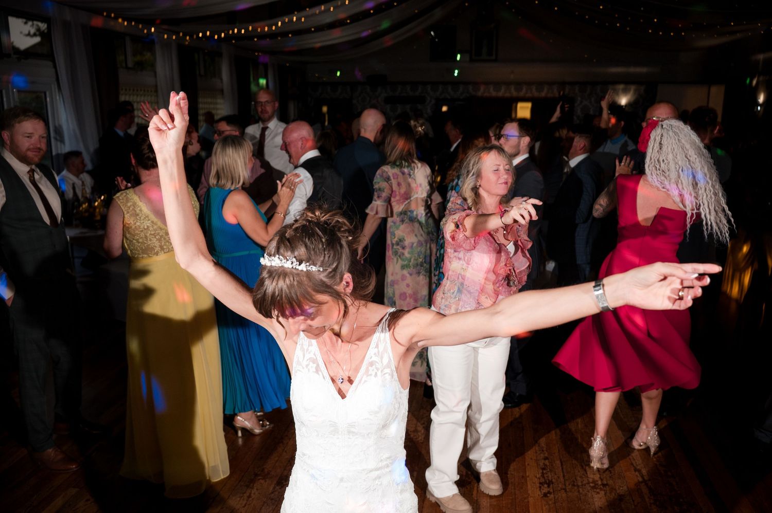 People dancing and celebrating at a lively party with string lights overhead.