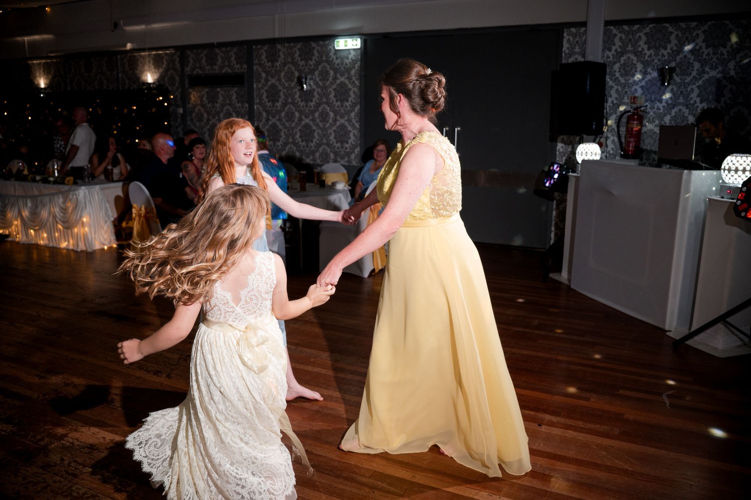 Two people in formal attire dance together on a wooden dance floor at a celebration event.