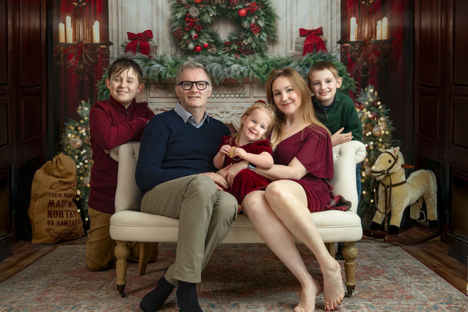 Family portrait in front of Christmas decorations with festive red and green decor.