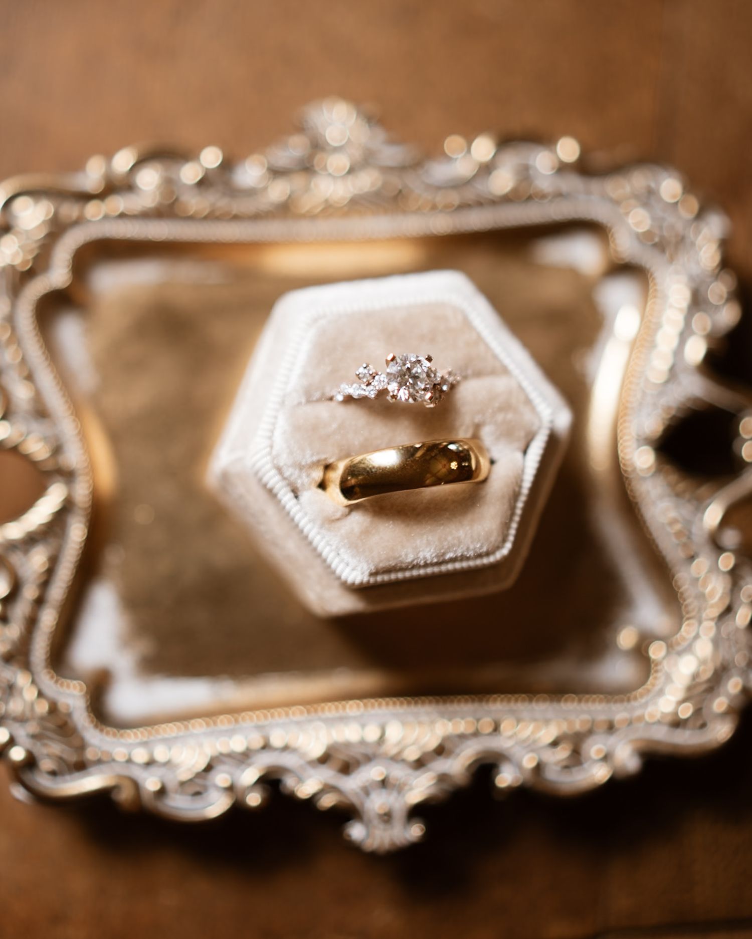 Wedding rings displayed in an ornate hexagonal box on a vintage silver tray with decorative details.