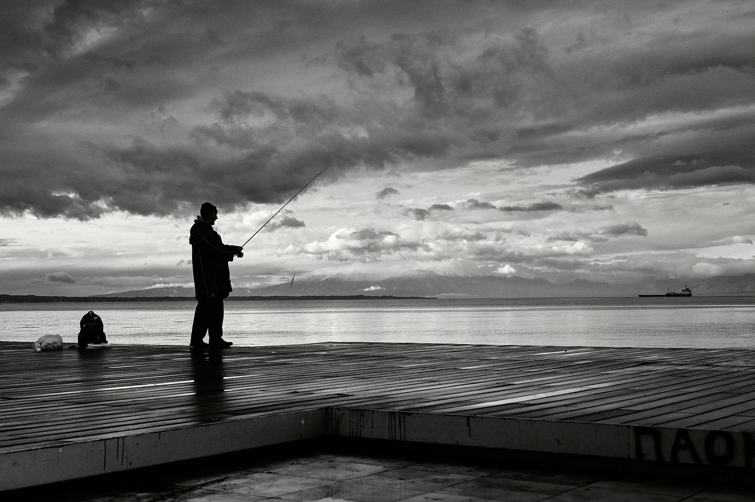 Dramatic black and white silhouettes of fishermen casting lines from a pier against a moody cloudy seascape.