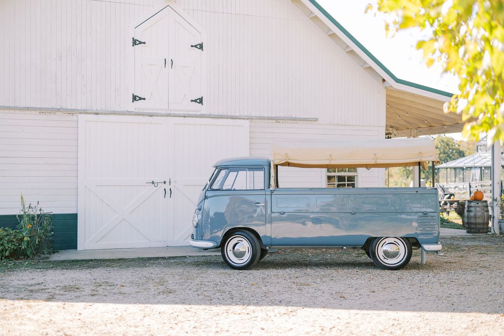A vintage blue Volkswagen van parked in front of a white barn on a sunny day.
