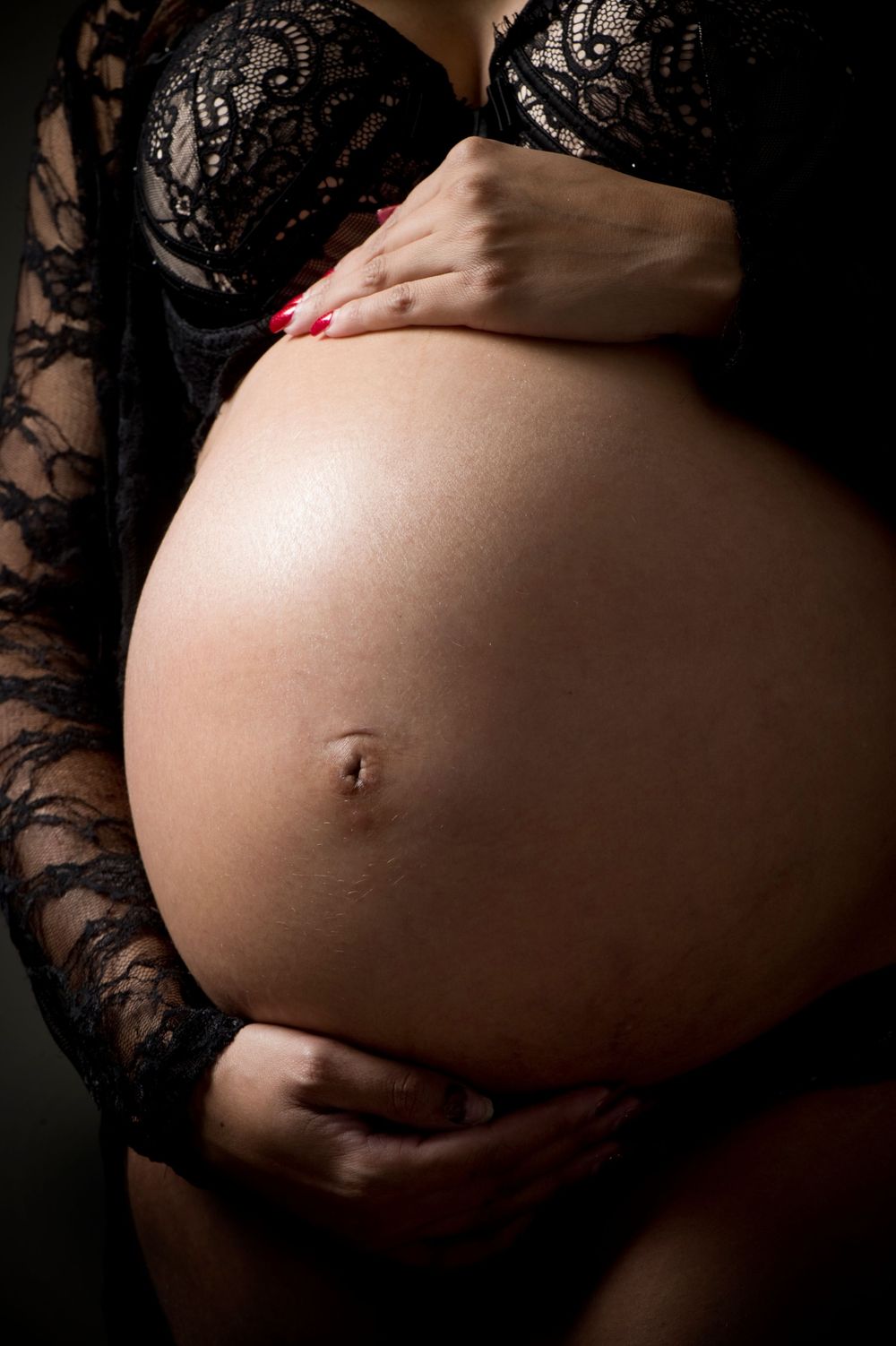 Close-up maternity photo showing pregnant belly with black lace detail and red nails.