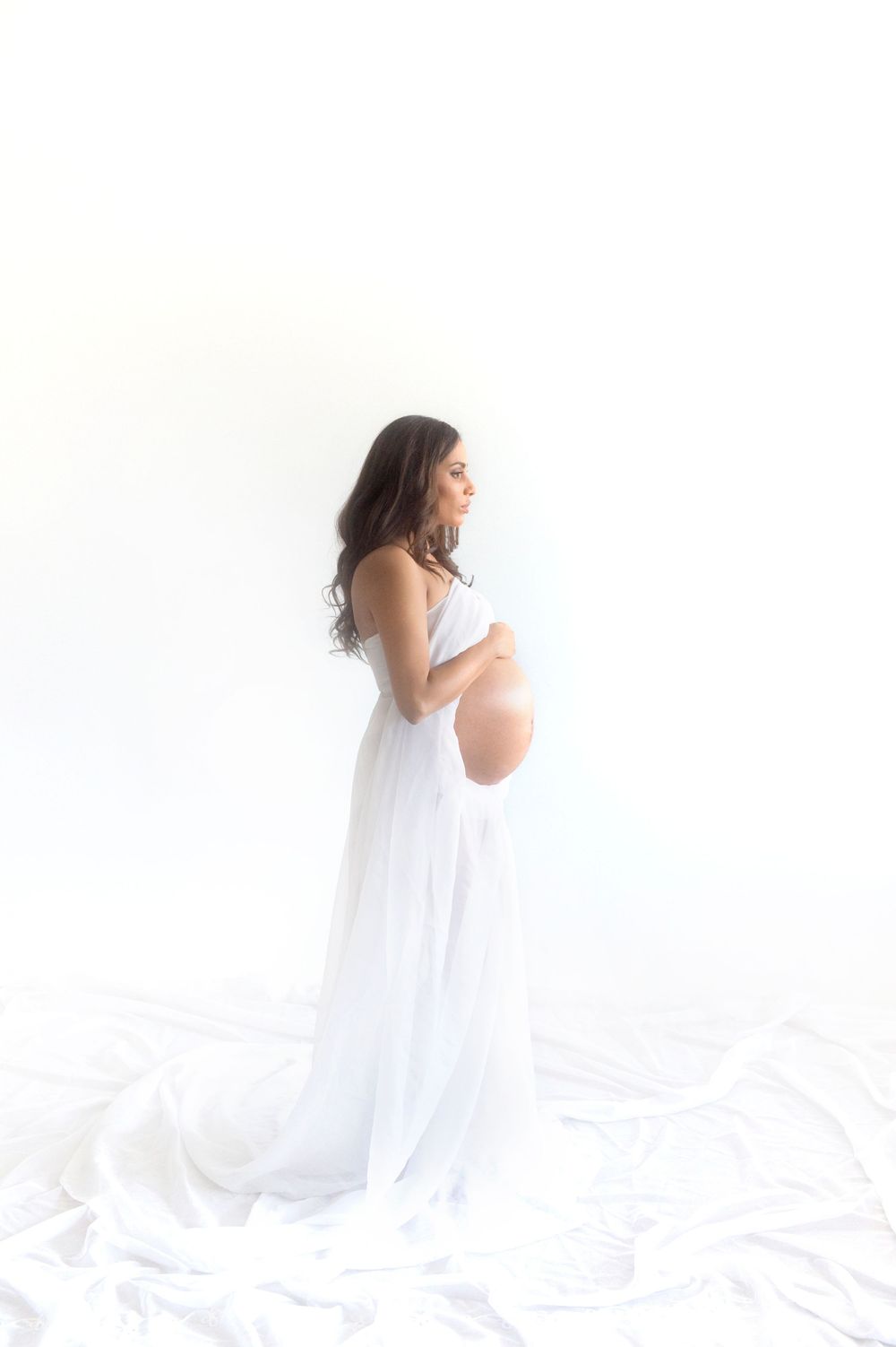 Ethereal maternity portrait in white flowing dress against bright background.