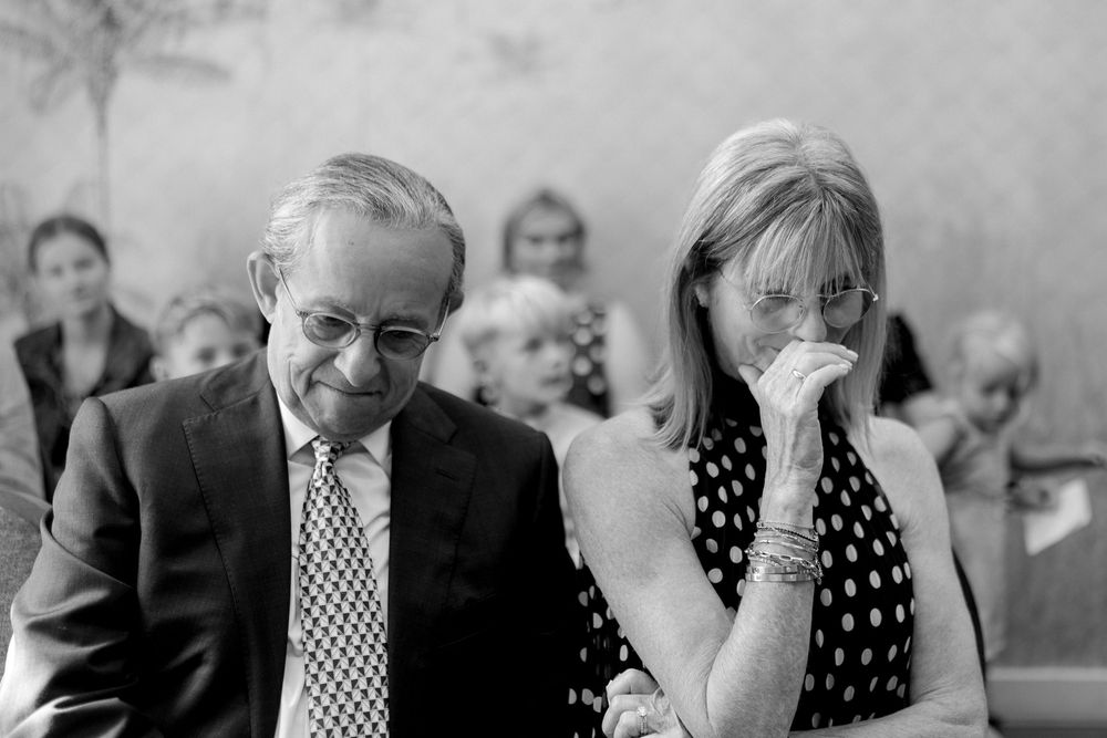 Emotional couple at wedding ceremony, man in suit and woman in polka dot dress wiping tears, black and white photo.