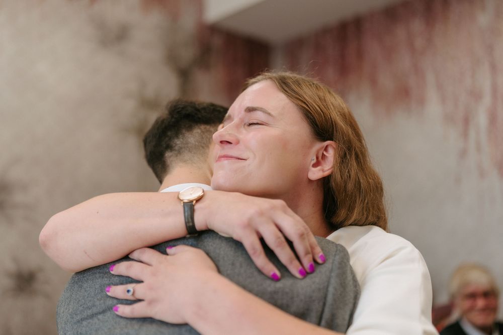 Two people share an emotional embrace while one wears a white sweater and watch.