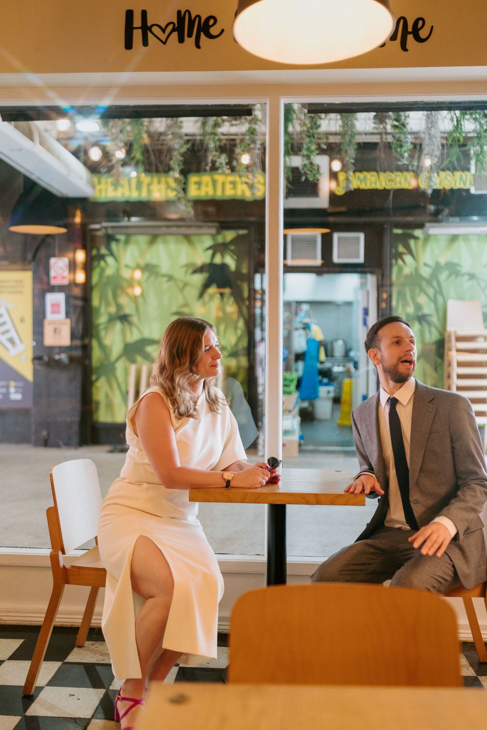 Couple in formal attire sitting at a table inside a casual restaurant with checkered floors and tropical decor.
