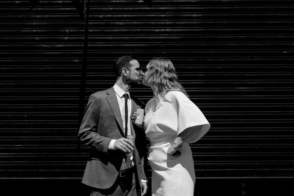 Black and white photo of a couple in wedding attire sharing a kiss against a striped wall backdrop.