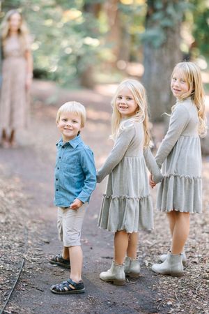 Three children pose together on a forest path wearing coordinated outfits.