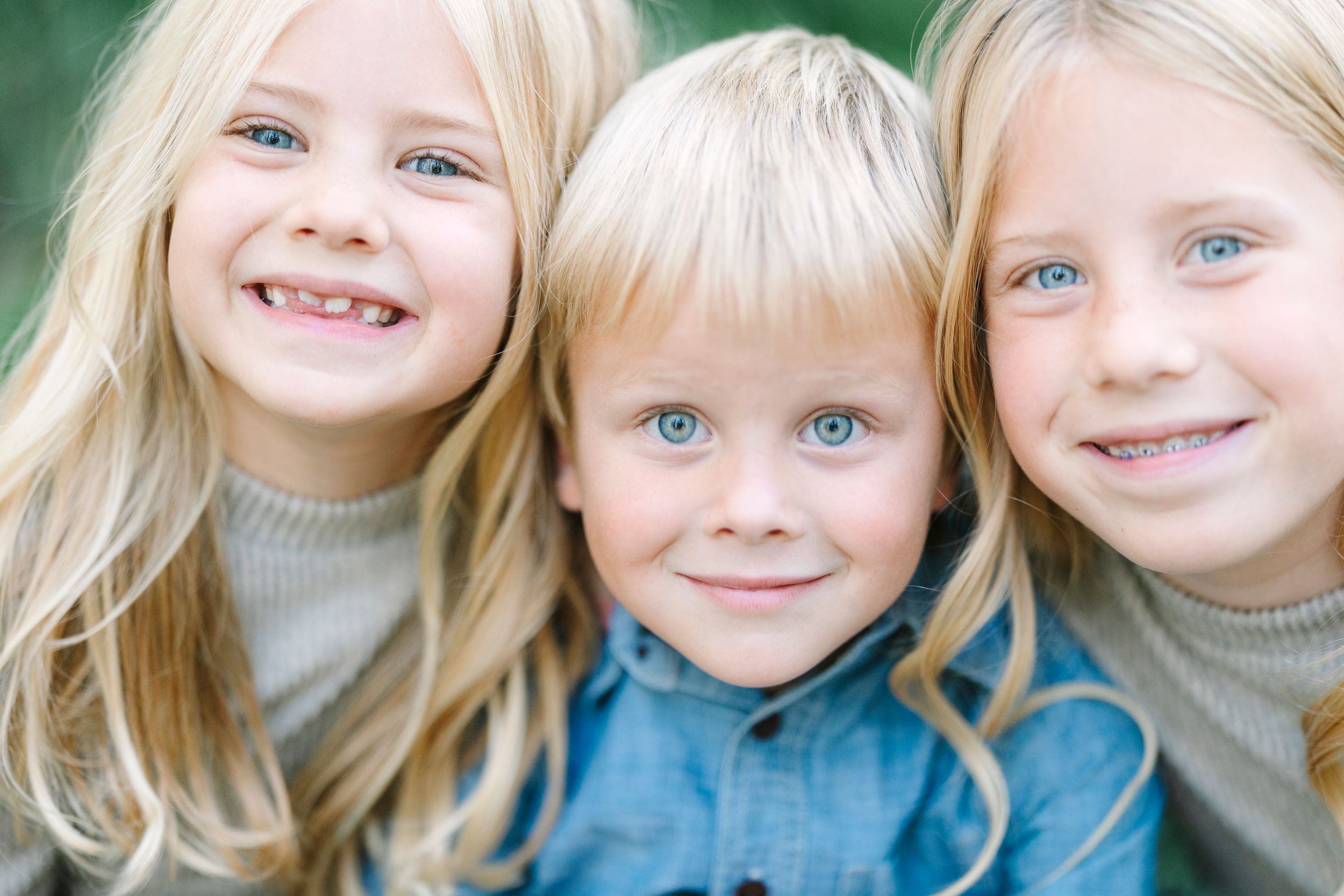 Three children smile together in a close-up outdoor portrait.