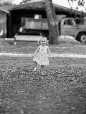 Black and white portrait of a small child walking on textured ground.