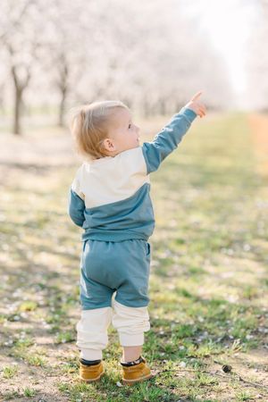 Toddler in blue outfit exploring outdoors while walking through a sunlit field.