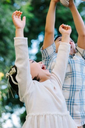 Children raising their arms joyfully against a blurred natural background.