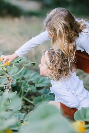 Two children in matching white tops exploring plants in garden setting.