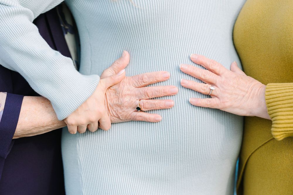 Close-up shots of hands gently cradling a pregnant belly in a gray top.