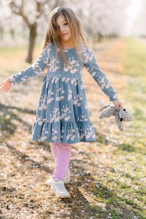 Young child in blue patterned dress twirling through fallen cherry blossoms.