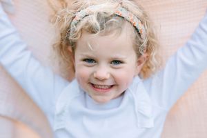 Close-up portrait showing bright smile and curly hair with white top.