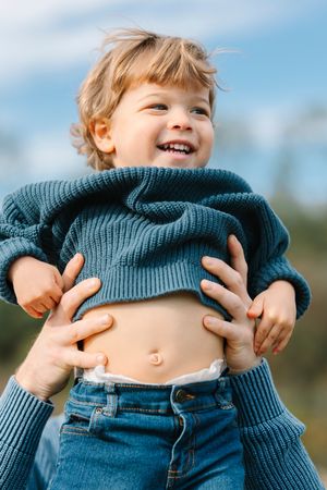 Child playfully lifting up a teal sweater showing their belly in a sequence of outdoor photos.