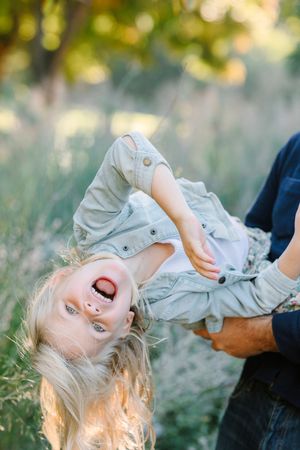 Playful upside-down moment captured in golden sunlight against blurred natural background.