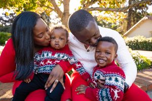 Family wearing matching red and white holiday sweaters embraces joyfully outdoors during golden hour.