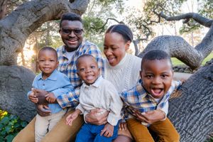 Joyful family members share genuine laughter and warm embraces while sitting together outdoors near a large tree.