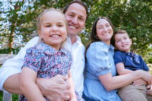 Family members sit together outdoors in a casual photoshoot against a green leafy background.