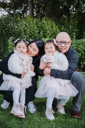 A family poses together outdoors on grass, wearing coordinated white and black outfits in a garden setting.