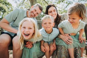 A joyful family shares candid laughs while laying together in green grass during a sunny outdoor photoshoot.