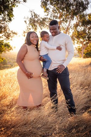 A loving family embraces in a golden field during sunset while wearing coordinated neutral-colored outfits.