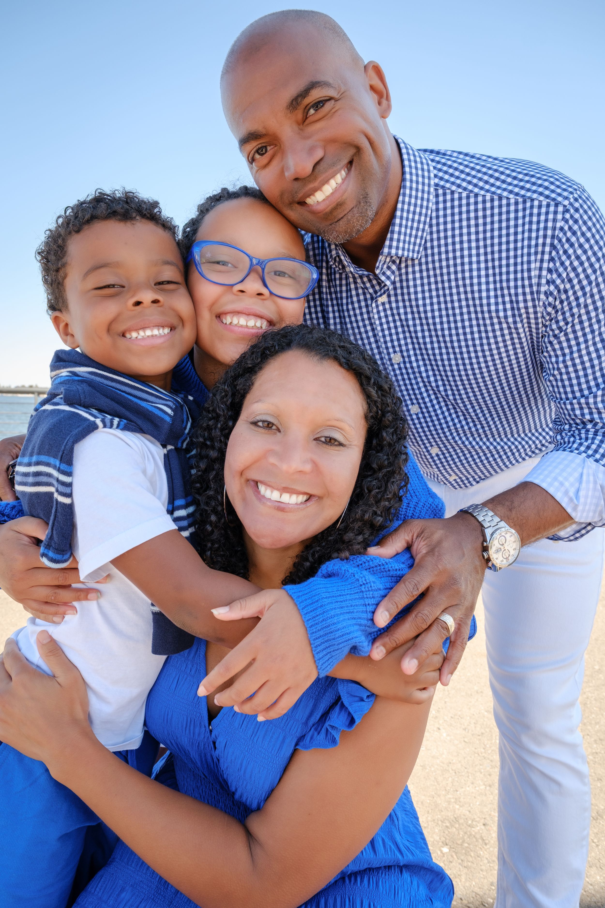 Happy African American family of four smiling together outdoors near water on a sunny day.
