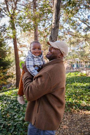 A joyful moment shared between two people in a brown jacket and plaid shirt outdoors among trees on a sunny day.