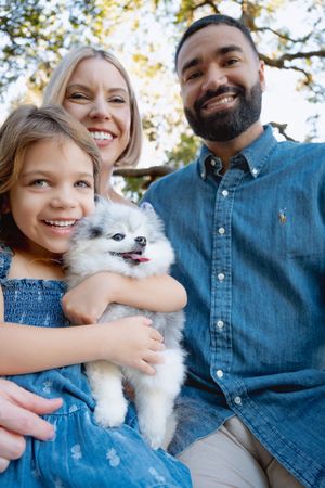 A happy family poses outdoors with their fluffy white Pomeranian dog in matching denim outfits.