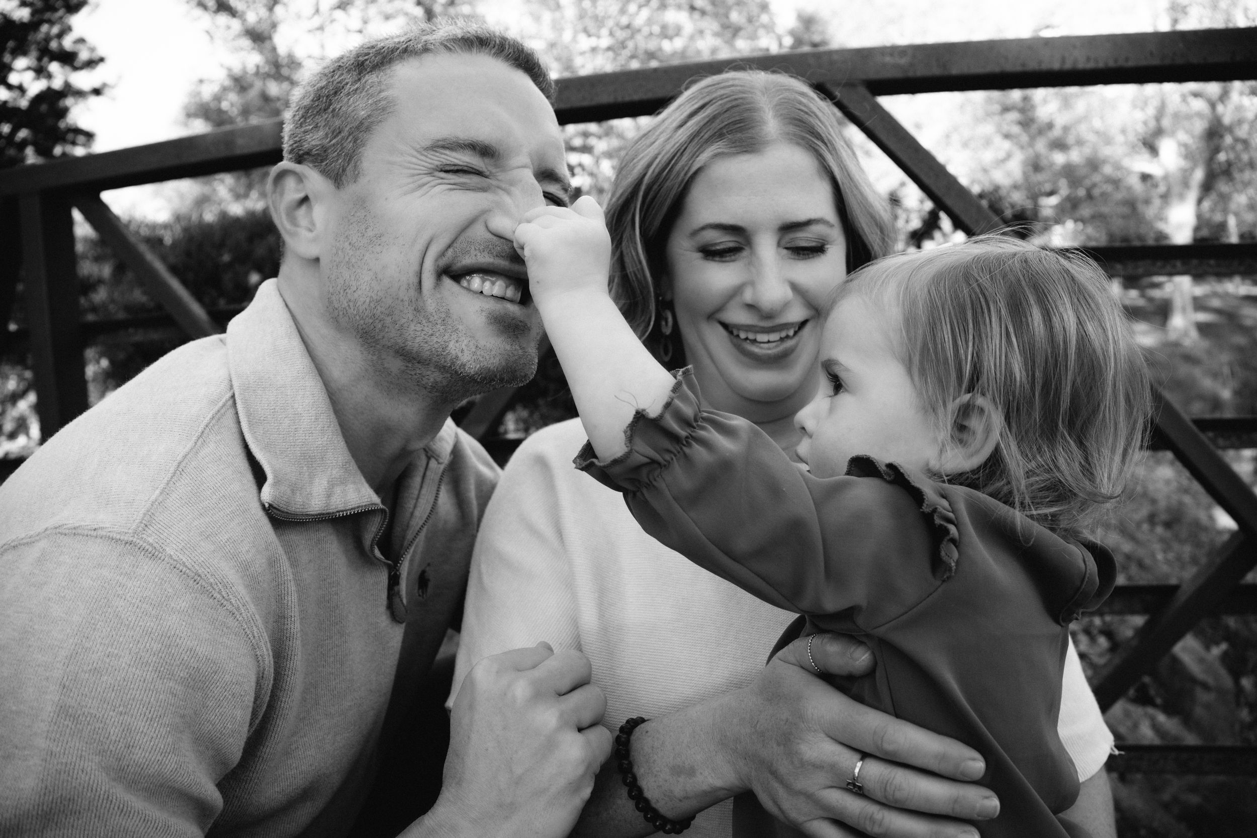 Black and white candid photos show a family laughing and sharing joyful moments together outdoors.