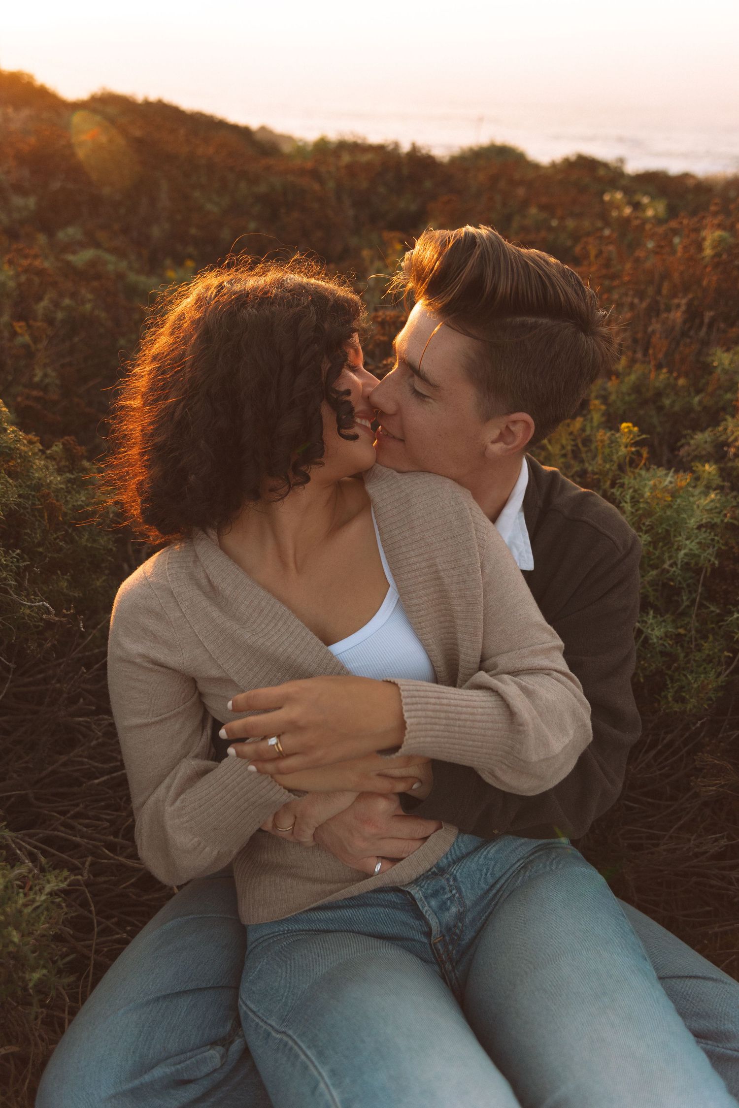 A couple shares an intimate embrace during golden hour against natural foliage.