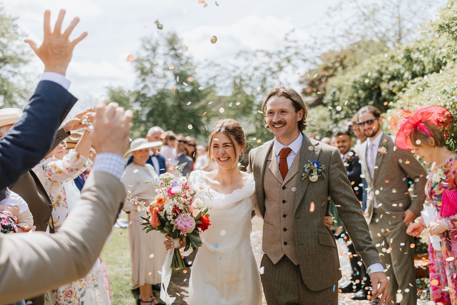 A group of wedding guests enjoying an outdoor reception with laughter and conversation in a natural setting.