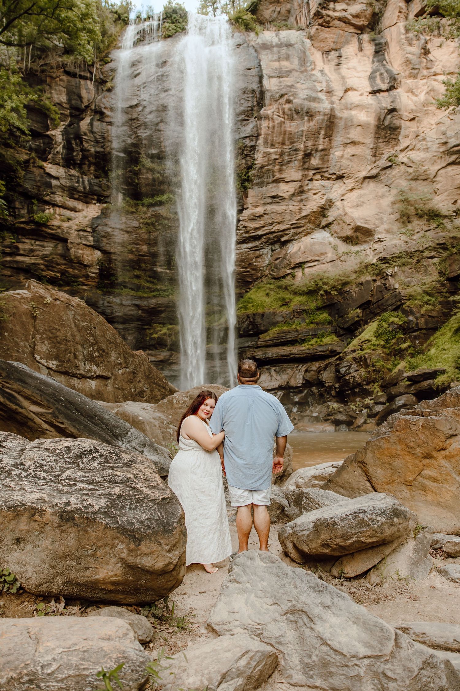 Romantic photoshoot at a scenic waterfall with rock formations in the background.