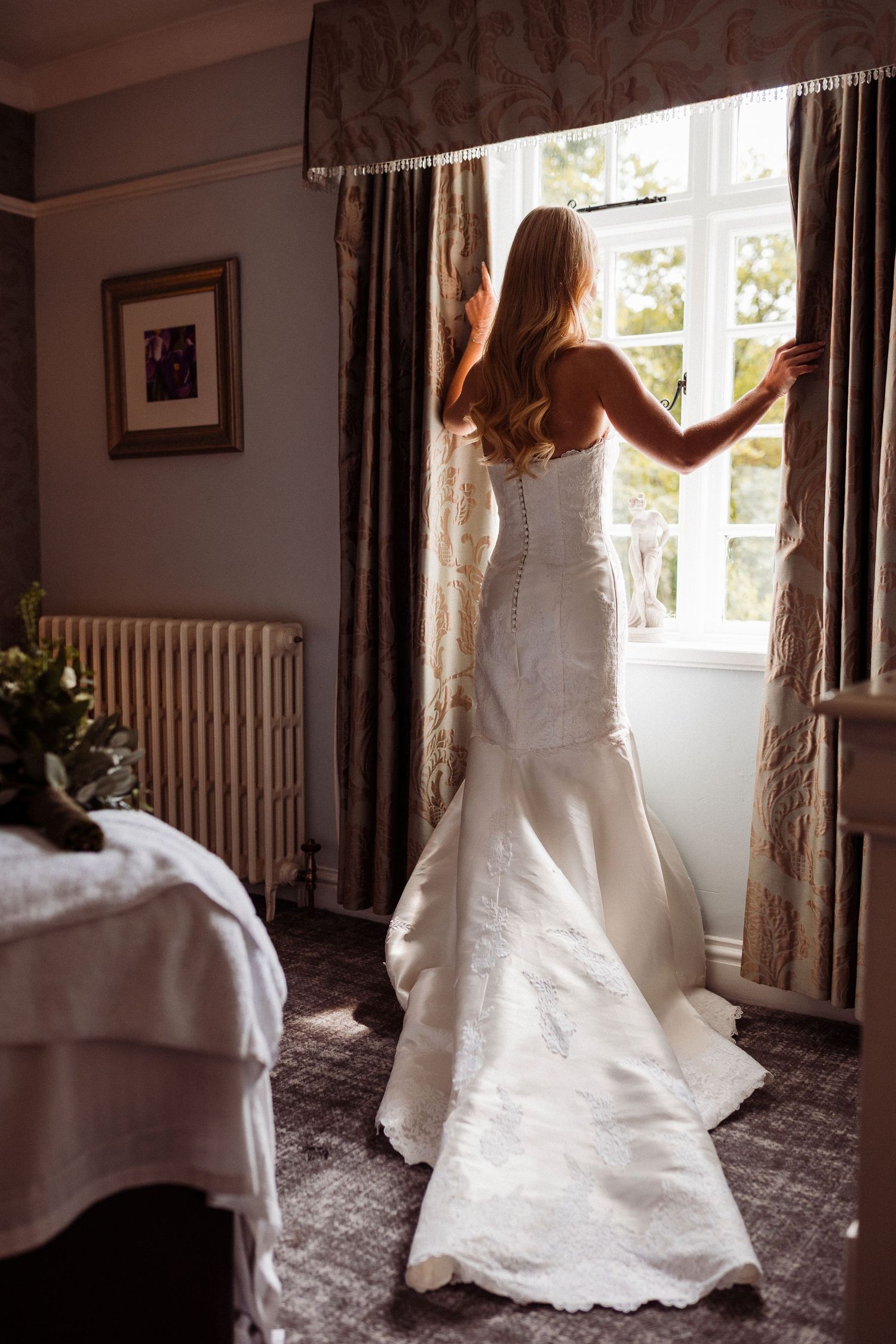 A bride in a flowing white wedding dress twirls gracefully in a sunlit room with vintage decor and curtains.